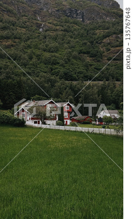 Red house in mountains. Green hills, clear sky, peaceful Nordic landscape.  135767648