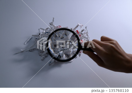 虫眼鏡でシュレッダーの紙屑を細かく調べる手 虫眼鏡でシュレッダーの紙屑を細かく調べる手 135768110