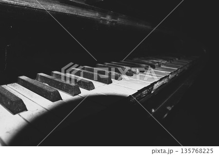 暗闇の中でスポットライトを浴びる古びたピアノの鍵盤のクローズアップモノクロ写真 暗闇の中でスポットライトを浴びる古びたピアノの鍵盤のクローズアップモノクロ写真 135768225