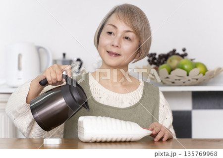 キッチンで湯たんぽにお湯を注ぐシニア女性 135769968