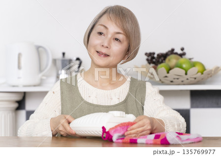 キッチンで湯たんぽにお湯を注ぐシニア女性 135769977