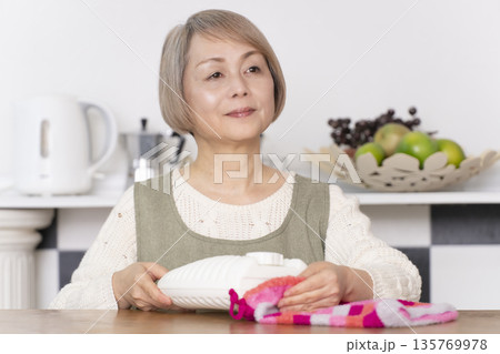 キッチンで湯たんぽにお湯を注ぐシニア女性 キッチンで湯たんぽにお湯を注ぐシニア女性 135769978