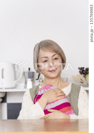 キッチンで湯たんぽにお湯を注ぐシニア女性 135769983