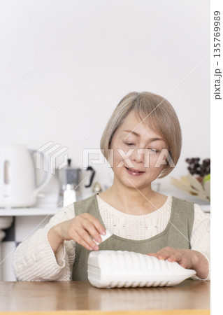 キッチンで湯たんぽにお湯を注ぐシニア女性 135769989