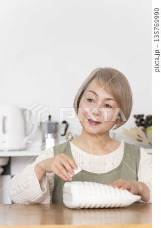 キッチンで湯たんぽにお湯を注ぐシニア女性 キッチンで湯たんぽにお湯を注ぐシニア女性 135769990