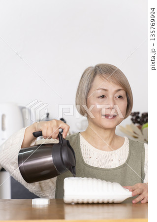 キッチンで湯たんぽにお湯を注ぐシニア女性 135769994