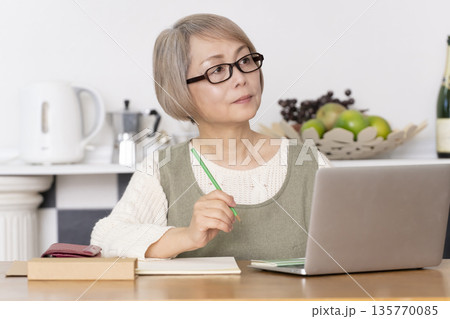 キッチンで家計簿をつけるシニア女性 135770085