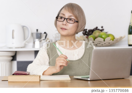 キッチンで家計簿をつけるシニア女性 135770086