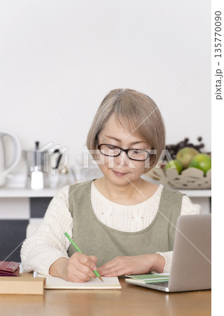 キッチンで家計簿をつけるシニア女性 135770090