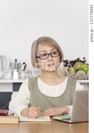 キッチンで家計簿をつけるシニア女性 135770092
