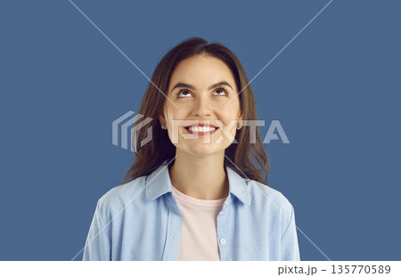 Portrait of smiling brunette woman in light blue shirt looking up on blue background. Portrait of smiling brunette woman in light blue shirt looking up on blue background. 135770589