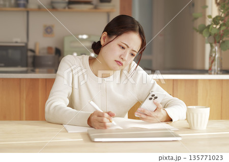 考え事をしながら書き物をする若い女性 考え事をしながら書き物をする若い女性 135771023