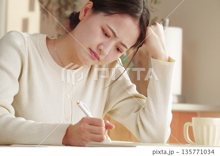 考え事をしながら書き物をする若い女性 考え事をしながら書き物をする若い女性 135771034