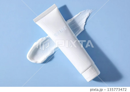 A smooth skincare cream dollop beside a white cosmetic tube on a soft blue background, showcasing texture and packaging 135773472