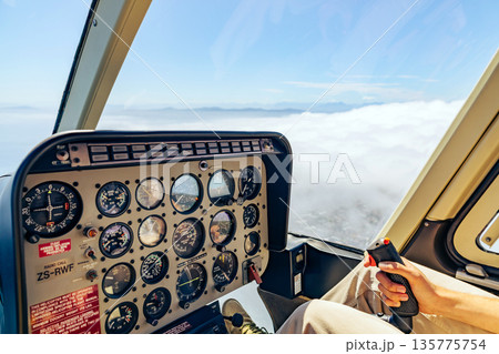 Man pilot operating helicopter control panel and joystick during flight, high above clouds. Luxury Cape Town tour. Aircraft cockpit view. Man pilot operating helicopter control panel and joystick during flight, high above clouds. Luxury Cape Town tour. Aircraft cockpit view. 135775754