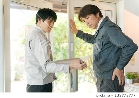 ガラス扉の前で打ち合わせする作業服の男性 135775777