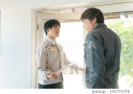 ガラス扉の前で打ち合わせする作業服の男性 135775778