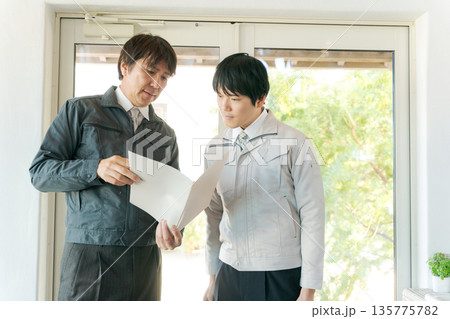 ガラス扉の前で打ち合わせする作業服の男性 135775782