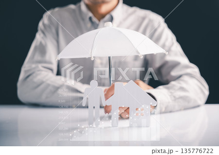 Protecting family property with insurance as safe investment is represented by a person sitting with paper shapes of house and person under an umbrella, securing property shown with overlaid charts Protecting family property with insurance as safe investment is represented by a person sitting with paper shapes of house and person under an umbrella, securing property shown with overlaid charts 135776722