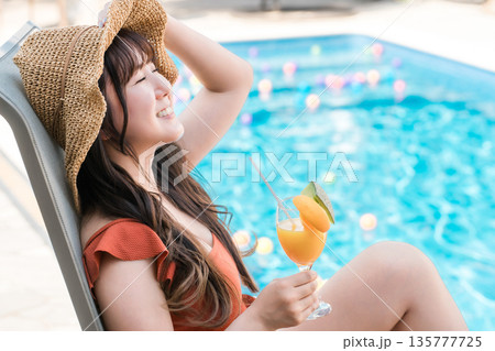 プールサイドのリクライニングチェアに座りトロピカルジュースを飲む水着姿の若いアジア人女性 プールサイドのリクライニングチェアに座りトロピカルジュースを飲む水着姿の若いアジア人女性 135777725
