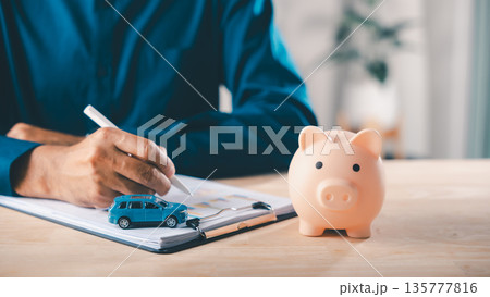 Man signs car finance contract near piggy bank, as money insurance and auto lease price help save documents and savings for bank loan and vehicle purchase planning process Man signs car finance contract near piggy bank, as money insurance and auto lease price help save documents and savings for bank loan and vehicle purchase planning process 135777816