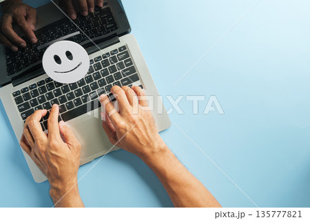 Client feedback and online review for customer satisfaction using laptop, hands typing on keyboard, happy face icon illustrates positive survey results 135777821