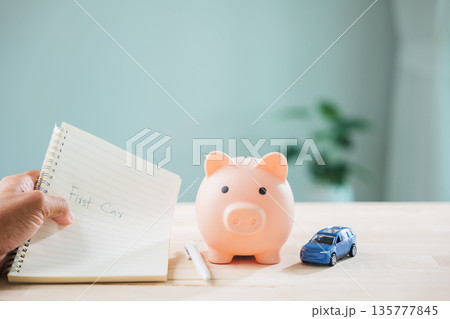 First car buying goal for money saving shown in notebook near piggy bank, blue toy model illustrates plan to save for loan, tax, cost, insurance, savings, pig, and finance budget First car buying goal for money saving shown in notebook near piggy bank, blue toy model illustrates plan to save for loan, tax, cost, insurance, savings, pig, and finance budget 135777845