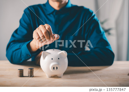 Man putting money into piggy bank shows global economy finance growth stock business concept, people save and invest for economic wealth and secure future financial stability Man putting money into piggy bank shows global economy finance growth stock business concept, people save and invest for economic wealth and secure future financial stability 135777847
