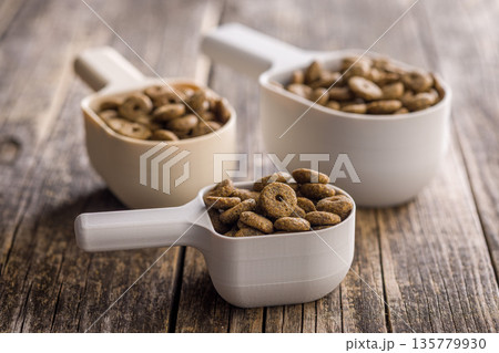 Dry kibble pet food. Dog or cat food in scoop on wooden table. 135779930