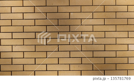 Light brown brick smooth wall in sunny soft lighting with spots of smooth shadows on the surface, geometric textured background of rectangular beige blocks 135781769