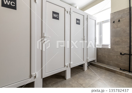 Row of modern white toilet stalls in a shared hostel bathroom Row of modern white toilet stalls in a shared hostel bathroom 135782437