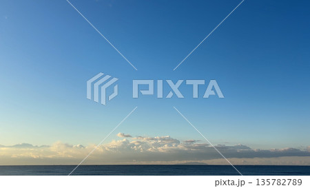朝のやわらかな光と帯状に広がる雲と穏やかな海 135782789