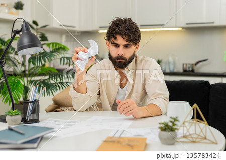 Indian man with many utility bills crumpling invoice frustrated about debt payment stress and worry Indian man with many utility bills crumpling invoice frustrated about debt payment stress and worry 135783424