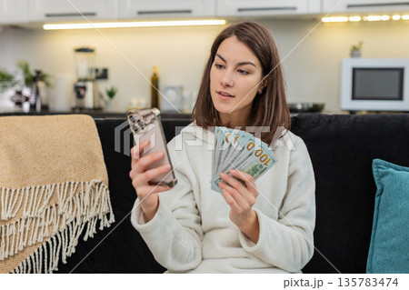 Woman counts money dollar cash checks rate on smartphone smiles plans dream buy salary savings bonus Woman counts money dollar cash checks rate on smartphone smiles plans dream buy salary savings bonus 135783474