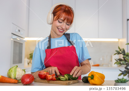 Young woman slices cucumber tomato on cutting board makes colorful salad and tastes fresh bite smile Young woman slices cucumber tomato on cutting board makes colorful salad and tastes fresh bite smile 135783496
