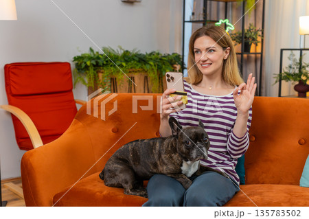Middle-aged woman with dog orders pet food in app pays by credit card on smartphone shows OK gesture Middle-aged woman with dog orders pet food in app pays by credit card on smartphone shows OK gesture 135783502