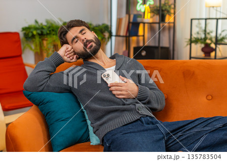 Indian man naps with smartphone wakes to loud alert important message quick look startled reaction Indian man naps with smartphone wakes to loud alert important message quick look startled reaction 135783504