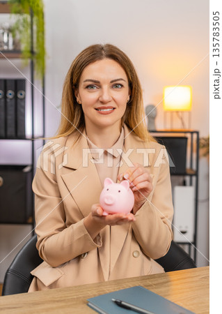 Businesswoman shakes empty piggy bank frowns drops coin inside makes save money gesture motivated 135783505
