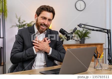 Middle-aged businessman streamer wearing headphones forms heart gesture after donation shouting wow 135783511