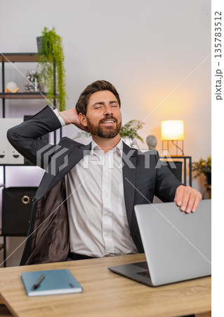 Middle-aged businessman finishes final report powers down laptop closes lid stretches smiles relaxed Middle-aged businessman finishes final report powers down laptop closes lid stretches smiles relaxed 135783512