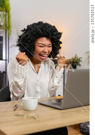 African American businesswoman excited celebrates laptop victory project approval and big game win African American businesswoman excited celebrates laptop victory project approval and big game win 135783513