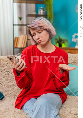 Young woman receiving bad news on smartphone screen, looking upset, disappointed shaking head sadly Young woman receiving bad news on smartphone screen, looking upset, disappointed shaking head sadly 135783566