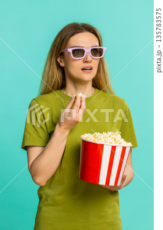 Adult woman in 3D glasses eating popcorn watching exciting movie with intense surprising storyline Adult woman in 3D glasses eating popcorn watching exciting movie with intense surprising storyline 135783575
