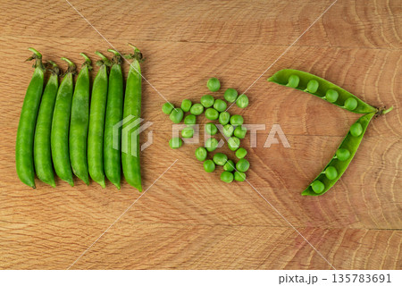 Whole stitches of peas and also separately grains of peas scattered on a wood board 135783691