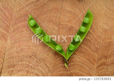 One opened stitch of peas, with grains of peas on a wooden board 135783693