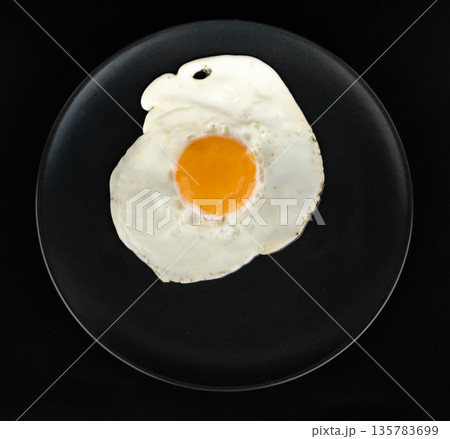 Fried egg lies on a black plate on a black background Fried egg lies on a black plate on a black background 135783699