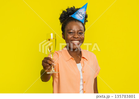 Black young woman raising champagne glass, party hat, birthday celebration, toast for special event Black young woman raising champagne glass, party hat, birthday celebration, toast for special event 135783801
