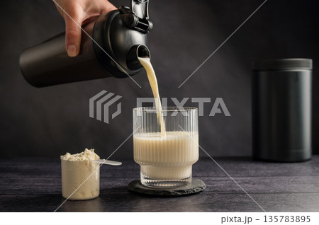 Protein drink. Pouring protein shake in a glass. Dark background. Body building, muscle growth and food supplement concept 135783895
