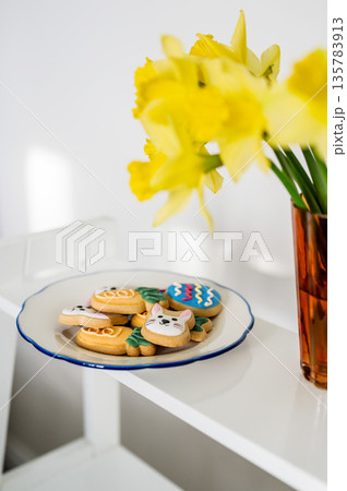 Easter spring background. Easter cookies with colourful icing: bunnies, carrots and eggs in a plate with bouquet of fresh. Bright and airy photo 135783913
