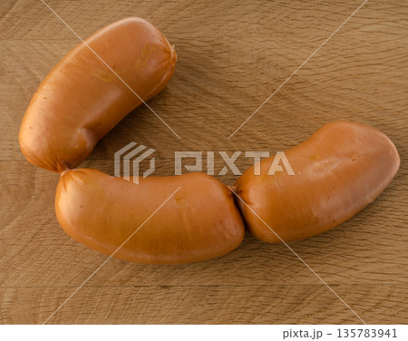 three boiled sausages, meat sausages on a wooden board three boiled sausages, meat sausages on a wooden board 135783941